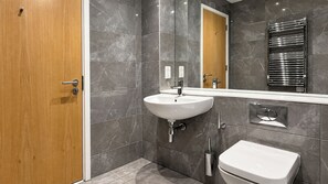 Ein modernes Badezimmer mit Holztür, Waschbecken in Weiß, Toilette und Spiegel.