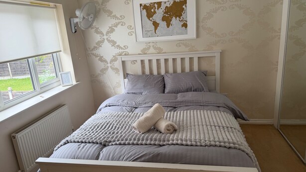A bedroom with a bed, a radiator, a window, a wall-mounted fan, and a world map on the wall. - North Manchester 2-Bed Apt, Sleeps 4 with Parking (Manchester)