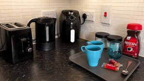 A kitchen with a toaster, kettle, coffee maker, and a tray with a coffee mug, a biscuit, and a spoon. - North Manchester 2-Bed Apt, Sleeps 4 with Parking (Manchester)
