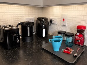 A kitchen with a toaster, kettle, coffee maker, and a tray with a coffee mug, a biscuit, and a spoon. - North Manchester 2-Bed Apt, Sleeps 4 with Parking (Manchester)