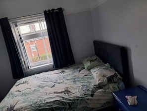 A bedroom with a bed, a window with curtains, and a blue bedside table.