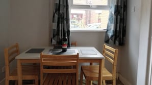 Un comedor con una mesa y cuatro sillas de madera, una botella de vino y un ventanal con cortinas.