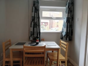 En matplats med ett bord och fyra trästolar, en vinflaska och ett fönster med gardiner.