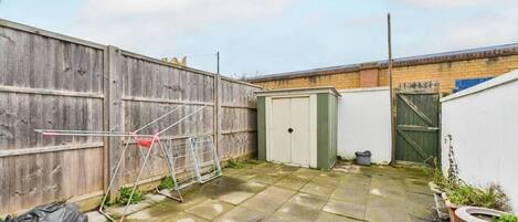 A backyard with a wooden fence, a green shed, and a metal clothesline.