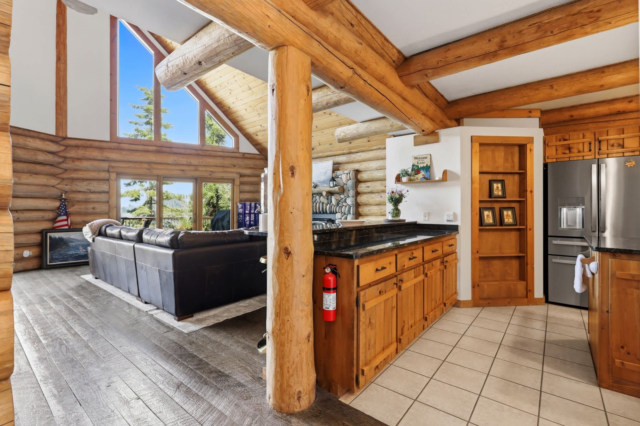 Ein Holzblockhaus-Innenraum mit Wohnbereich, Küche und einem großen Fenster mit Blick auf viel Grün.