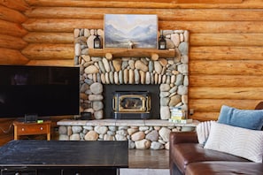 A log cabin interior with a stone fireplace, a television, and a leather sofa. - Cozy's Lakefront Lodge | Luxury Log Cabin (Harrison)