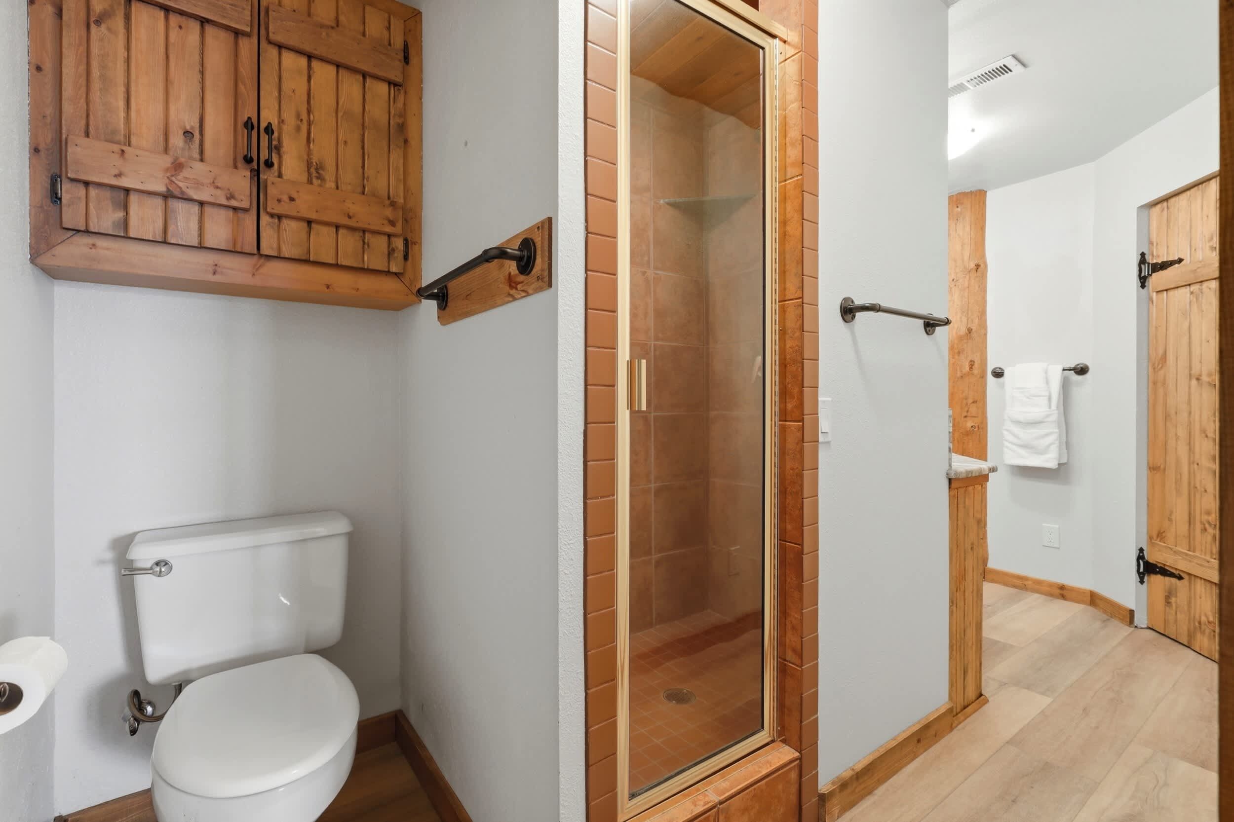 A bathroom with a wooden cabinet, a glass-enclosed shower, and a white toilet.