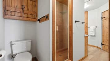 A bathroom with a wooden cabinet, a glass-enclosed shower, and a white toilet.
