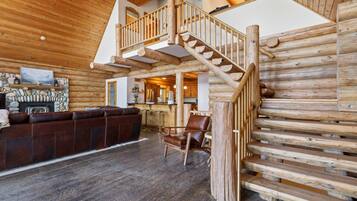 Ein rustikales Blockhaus-Interieur mit einer Holztreppe, einem Steinkamin, einer Ledersofa und einer Bar.