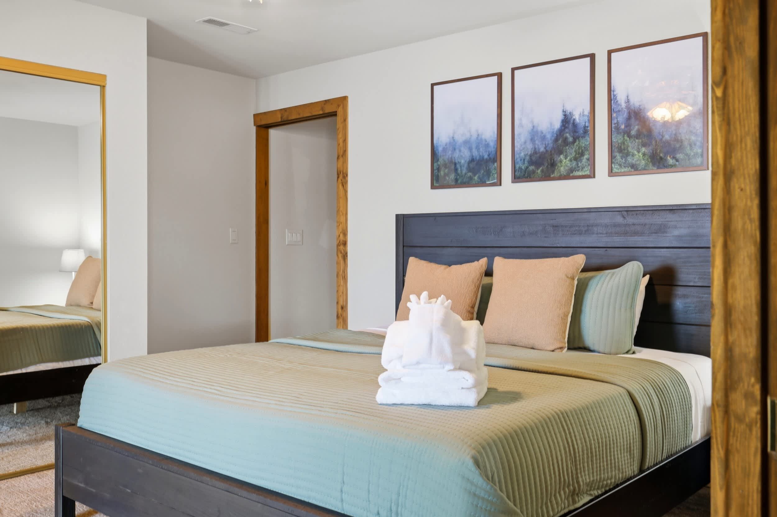Ein Hotelzimmer mit einem Bett, einem Holz-Kopfteil, einem Spiegel und drei gerahmten Bildern an der Wand.