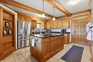 A kitchen with wooden cabinets, a stainless steel refrigerator, a microwave, and a coffee maker. - Cozy's Lakefront Lodge | Luxury Log Cabin (Harrison)
