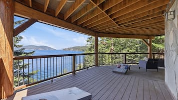 Een houten terras met uitzicht op een meer en bergen, een barbecue en zitplaatsen buiten.