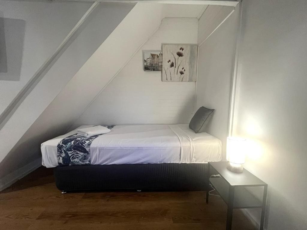 Una stanza piccola e poco illuminata con un letto, un comodino e un quadro appeso al muro.