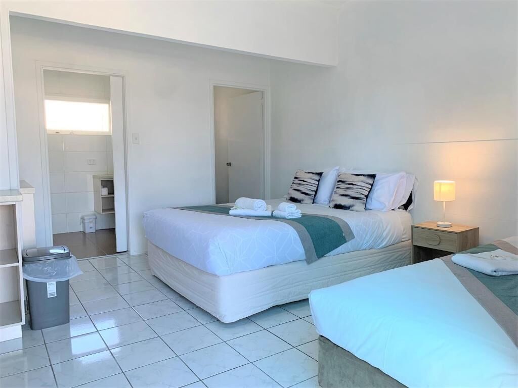 A hotel room with a large bed, a bedside table, a lamp, and a trash bin.