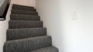 Una escalera con peldaños alfombrados que lleva a un rellano con un aplique en la pared.