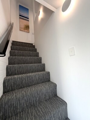 A staircase with carpeted steps leading to a landing with a wall-mounted light fixture. - Aqua Blue Motel (Biggera Waters)