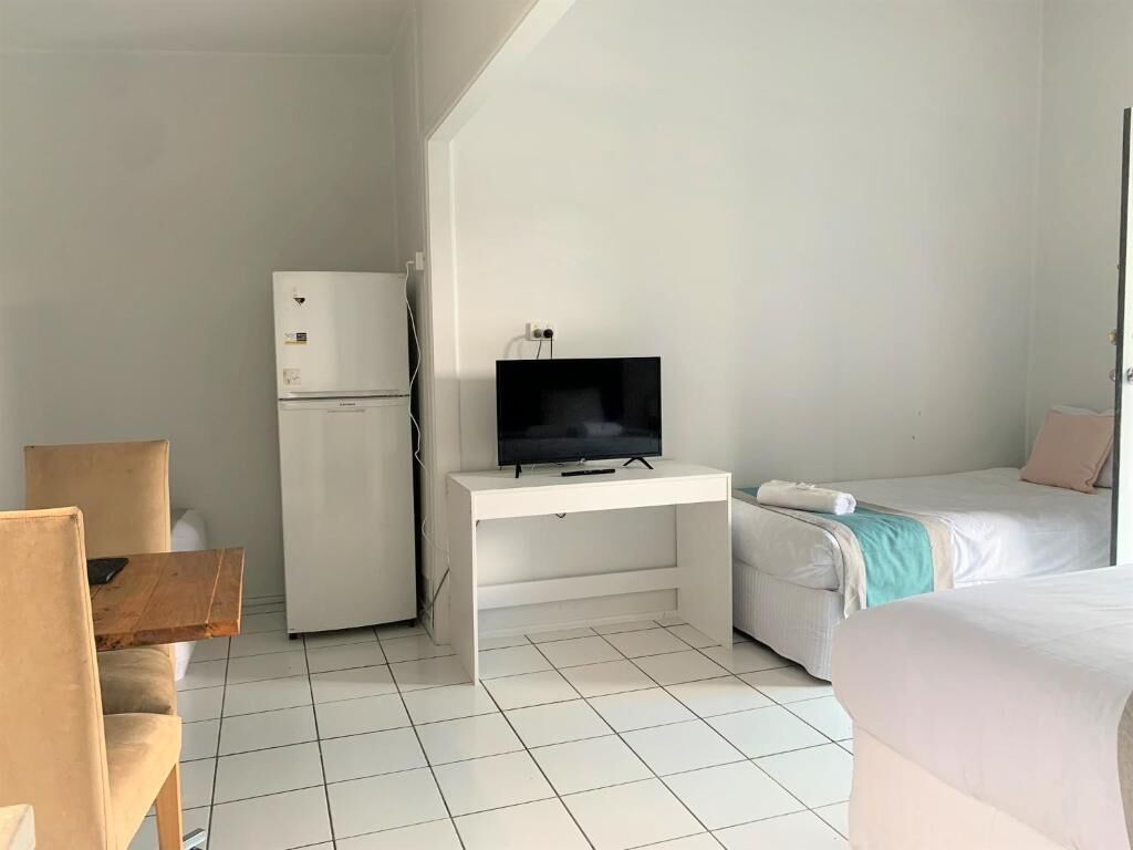 A hotel room with a bed, a desk with a television, a refrigerator, and a chair.