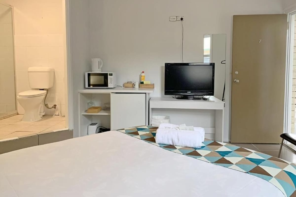Una habitación de hotel con una cama, televisión, microondas y un inodoro.