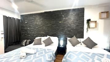 A hotel room with two beds, a dark stone accent wall, a small bedside table with a lamp, and a window with curtains.