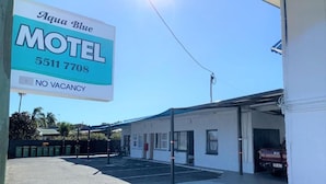 Un motel con un cartello che indica 'Aqua Blue Motel' e un numero di telefono. L'edificio ha un tetto piatto e un'area di parcheggio coperta.