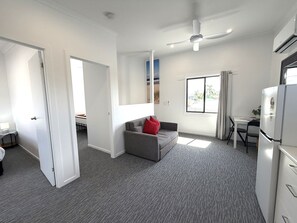 A compact living space with a grey sofa, a ceiling fan, a window with a view, and a kitchenette.