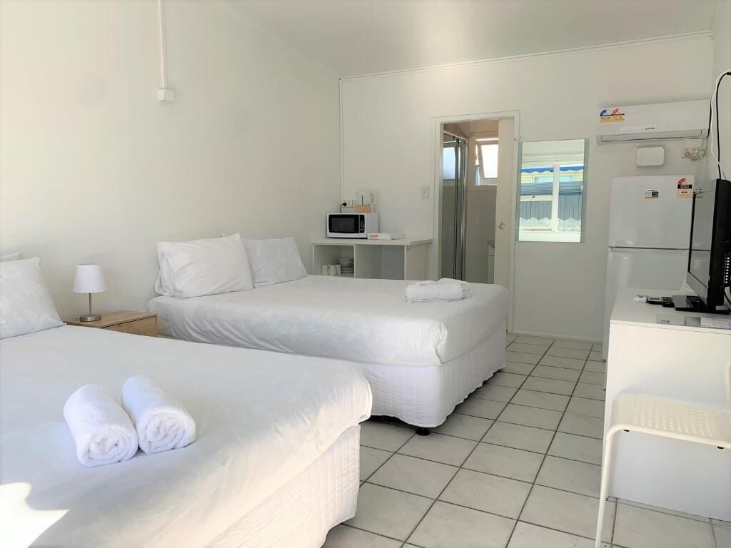 A hotel room with two beds, a microwave, a refrigerator, and a TV.