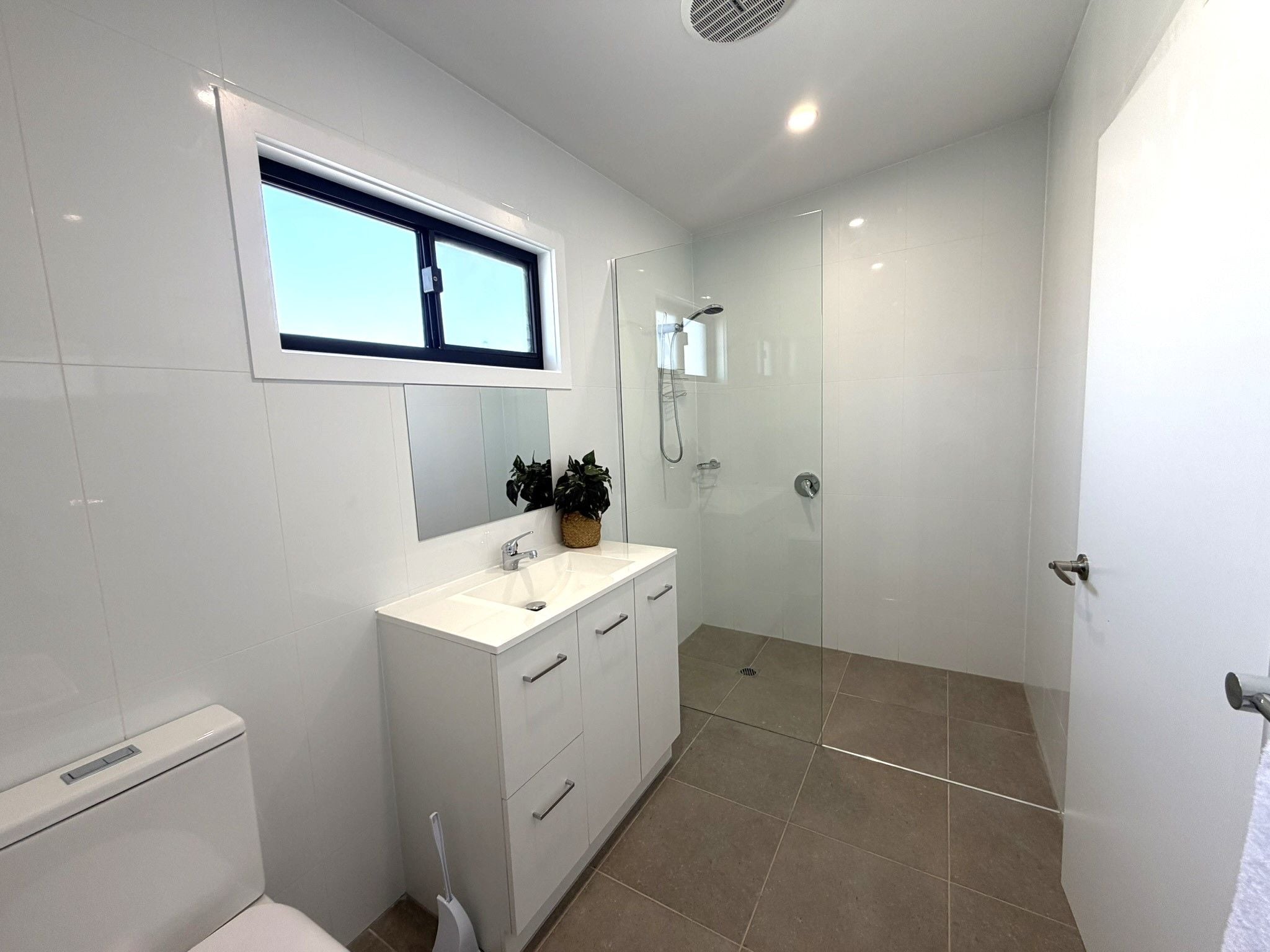 A modern bathroom with a toilet, a sink, a shower, and a mirror.