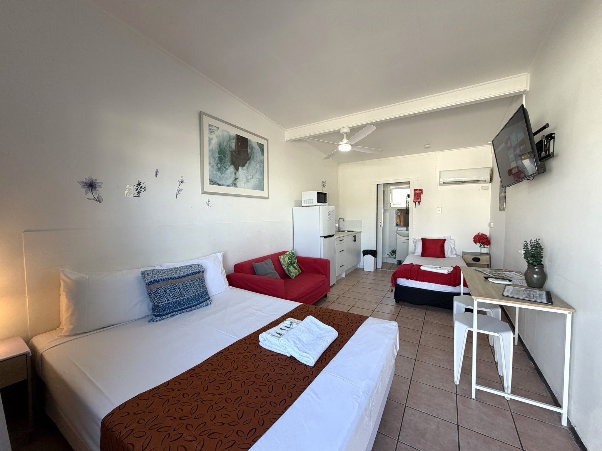 Une chambre d’hôtel avec un lit, un canapé rouge, un bureau avec un ordinateur et un téléviseur fixé au mur.