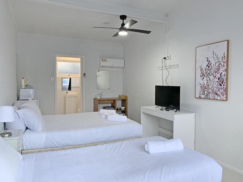 A hotel room with two beds, a desk with a computer, a ceiling fan, and a painting on the wall.