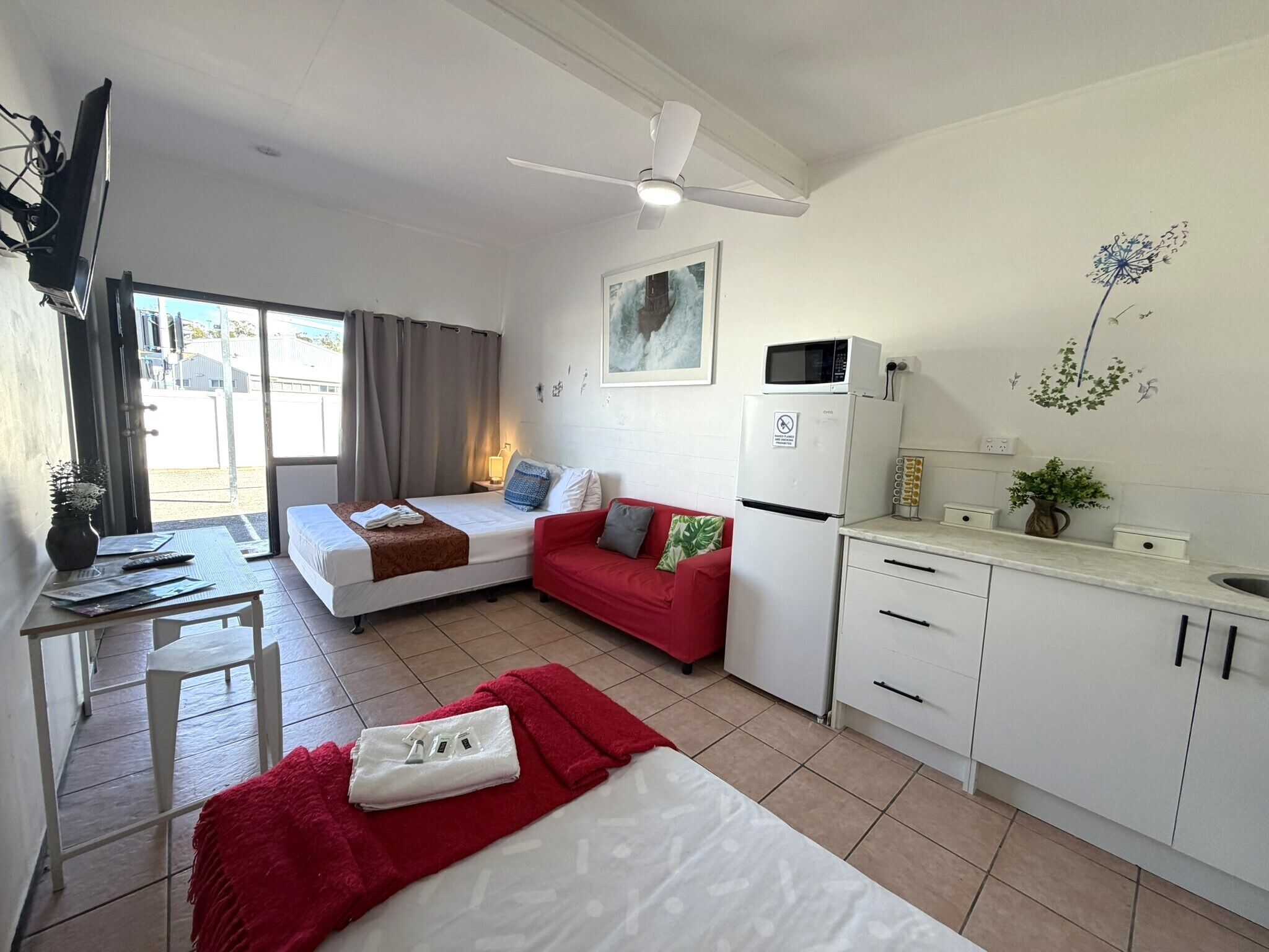 A compact hotel room with a bed, a red sofa, a kitchenette, and a dining area.