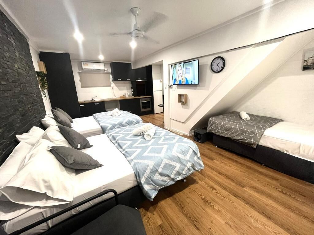 A modern bedroom with two beds, a kitchenette, a TV, and a clock on the wall.