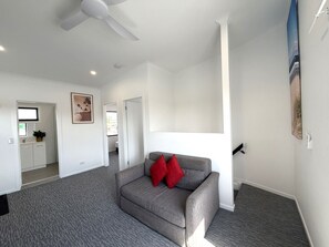 A modern living room with a grey sofa, red cushions, a ceiling fan, and a view of a bathroom and kitchen. - Aqua Blue Motel (Biggera Waters)