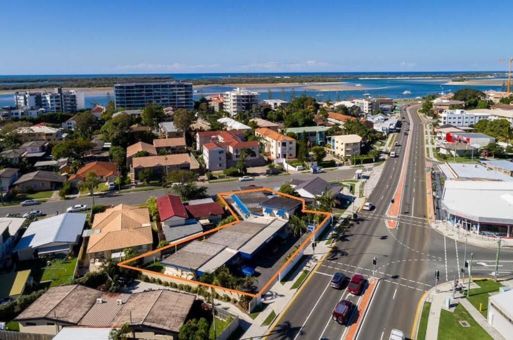 An aerial view of a coastal town with a main road, buildings, and a beach in the background.