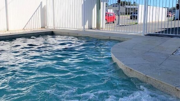 A swimming pool with a fence, a motel sign, and a red car in the background.
