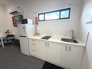A compact kitchenette with a refrigerator, microwave, sink, and a small window above the countertop. - Aqua Blue Motel (Biggera Waters)
