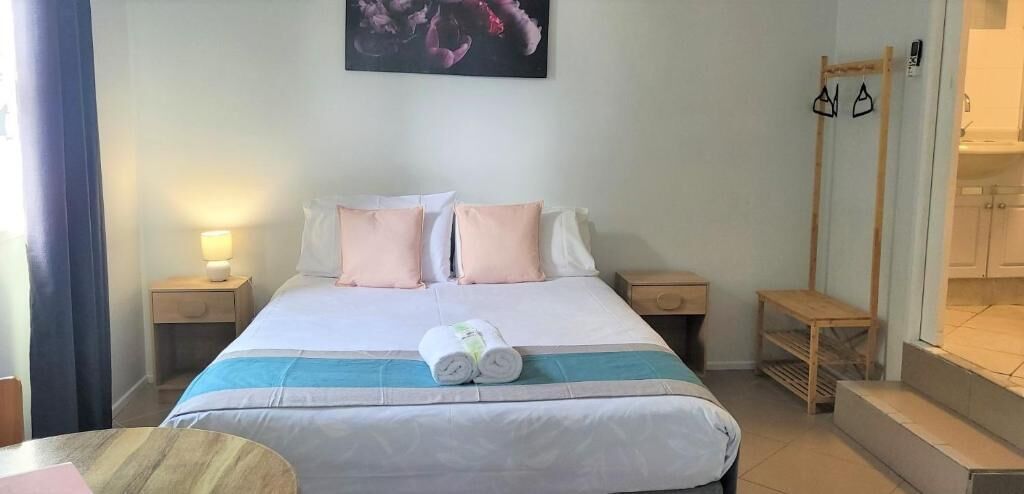 Ein Hotelzimmer mit einem Bett, Nachttischen, einer hölzernen Bank und einem Wandhaken für Kleidung.