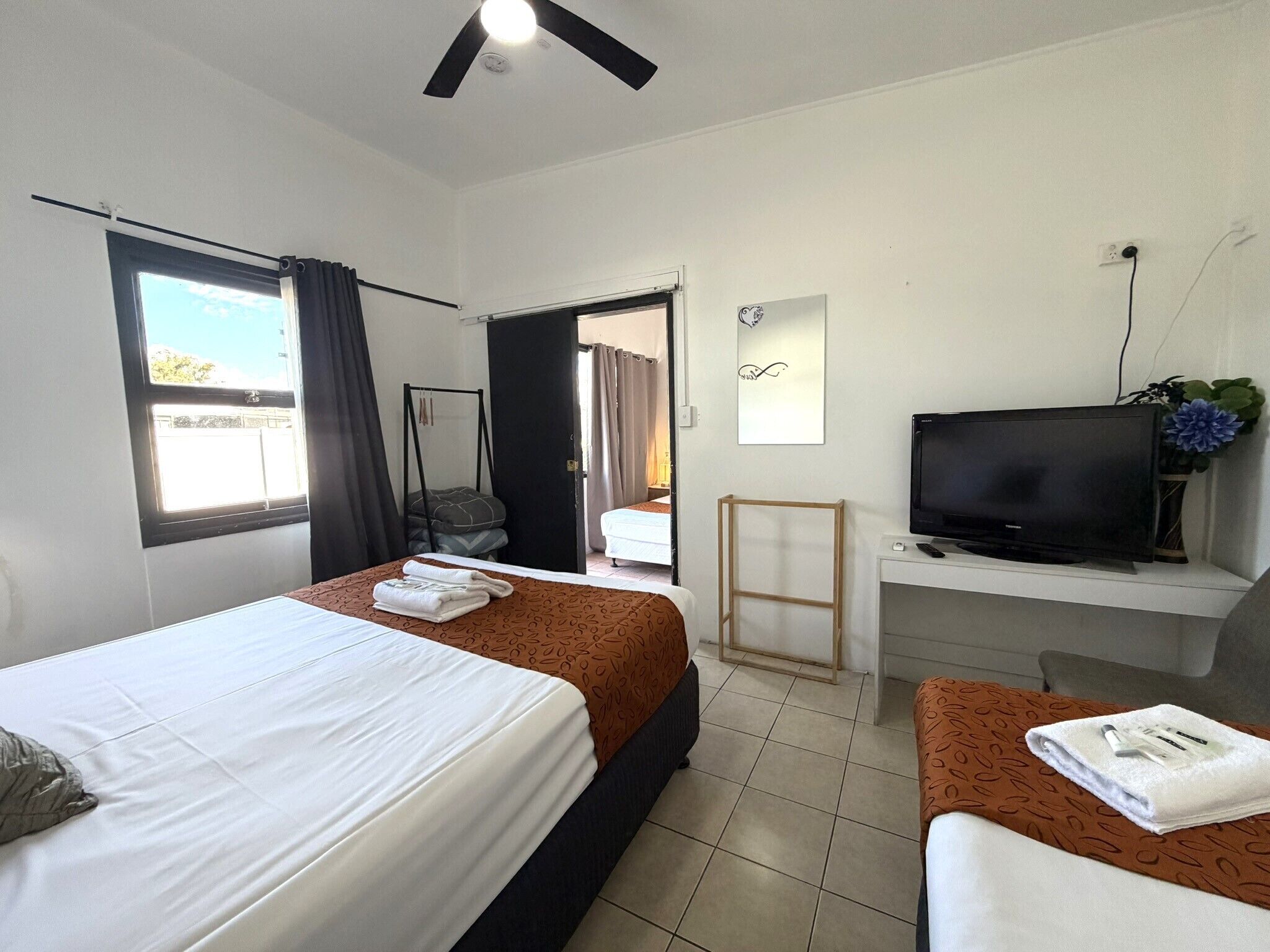 A hotel room with two beds, a desk with a TV, and a view of the outdoors.