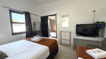 A hotel room with two beds, a desk with a TV, and a view of the outdoors.