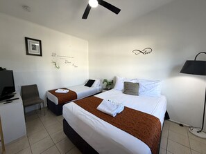 A hotel room with two beds, a desk with a TV, a chair, and a ceiling fan.