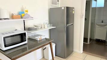 A compact kitchen with a microwave, a stainless steel refrigerator, and a small countertop.