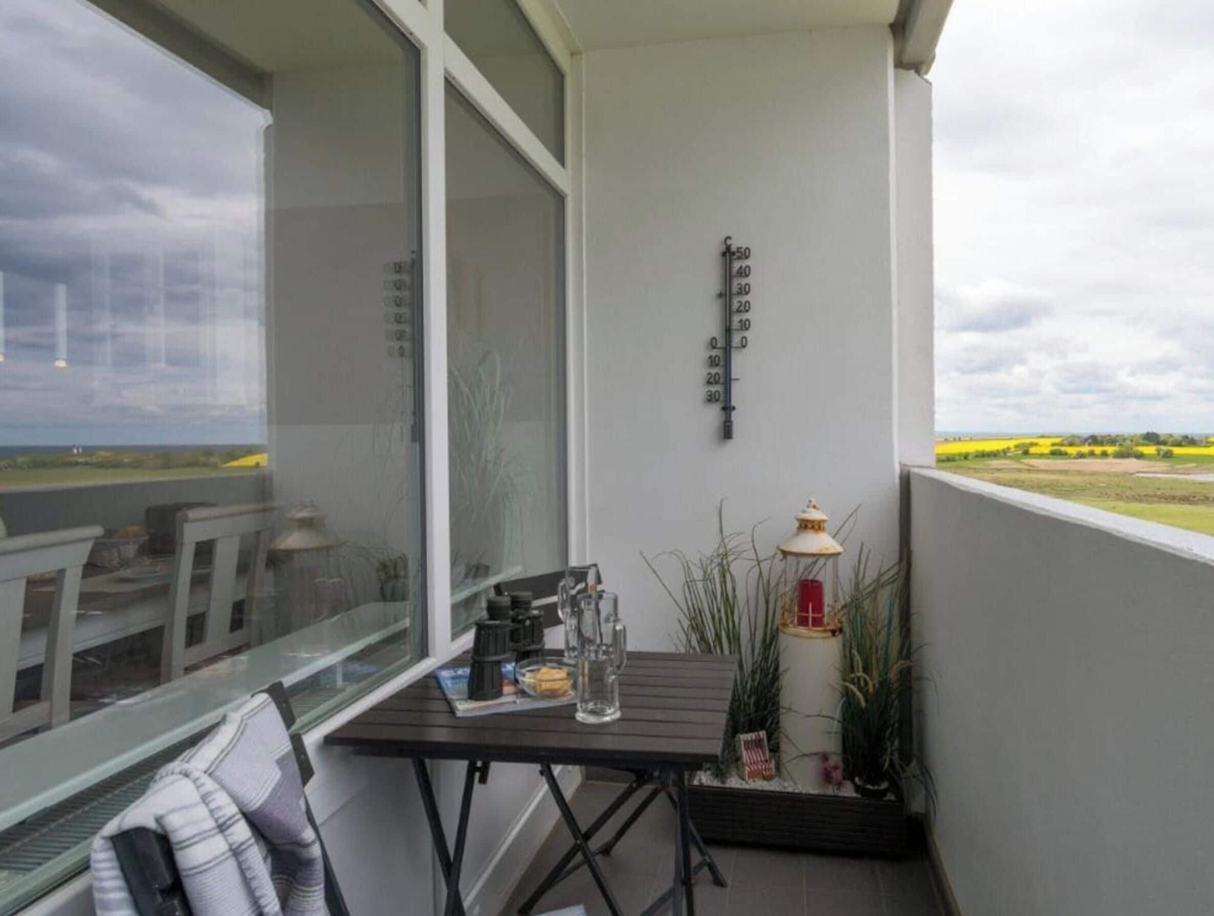 Ein Balkon mit Tisch, Stühlen, einem Thermometer und einer Laterne.