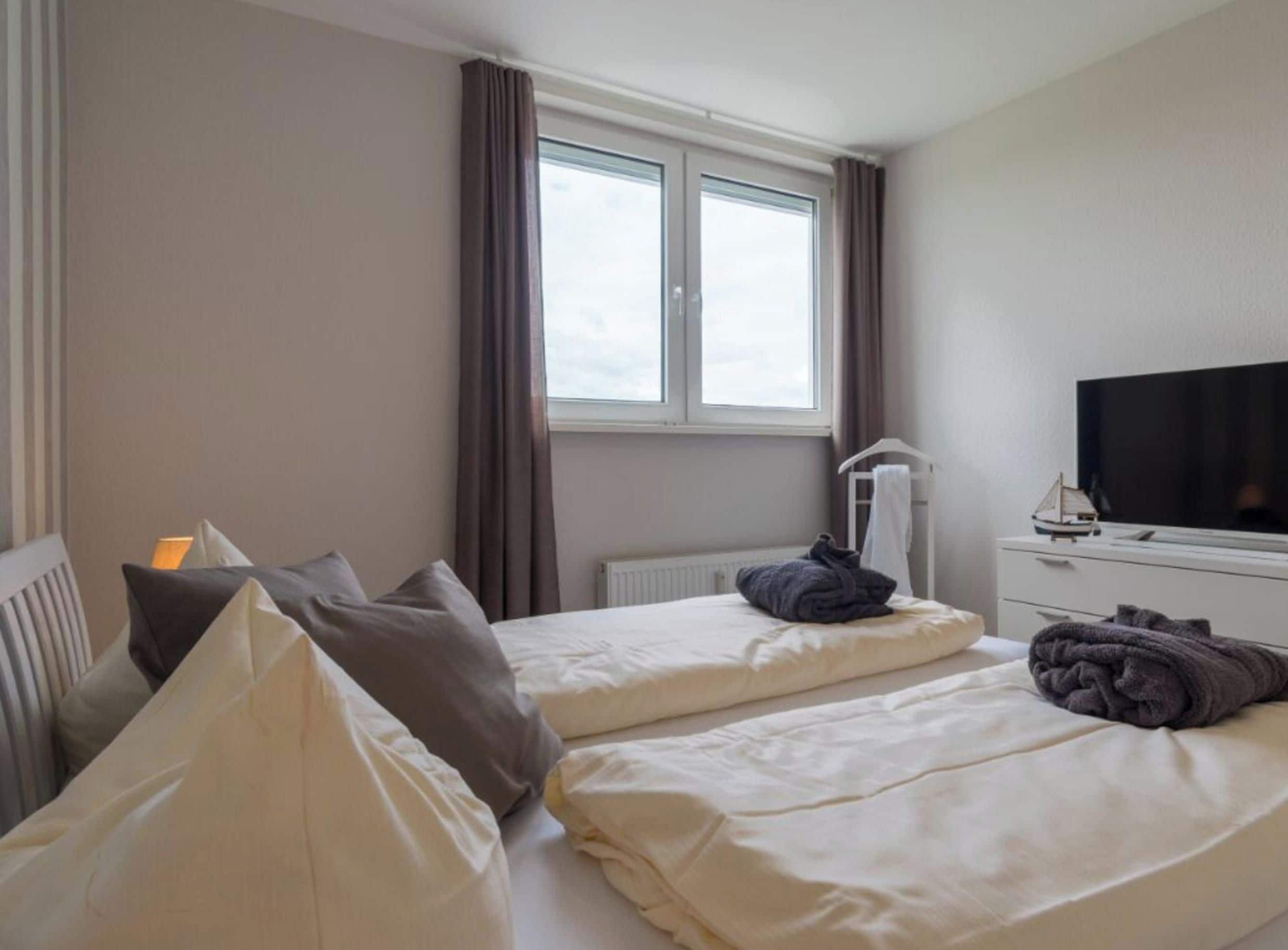 A hotel room with two beds, a television, a radiator, and a window with curtains.