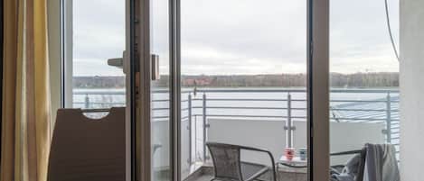En balkon med udsigt over vand og en fjerntliggende kystlinje, møbleret med en stol og et lille bord.