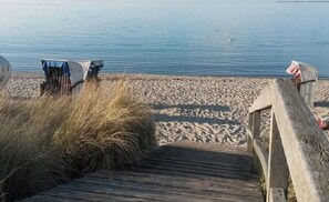Un paseo marítimo de madera que conduce a una playa arenosa, con aguas tranquilas al fondo.
