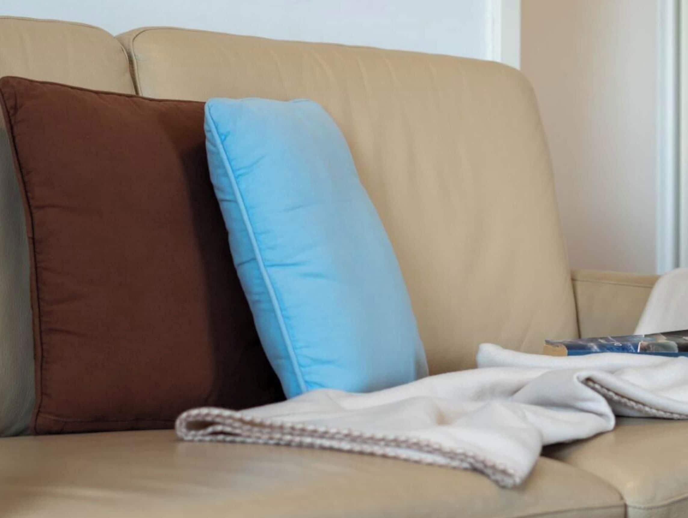 Ein beiges Sofa mit zwei Kissen, einem braunen und einem blauen, und einer weißen Decke darauf.