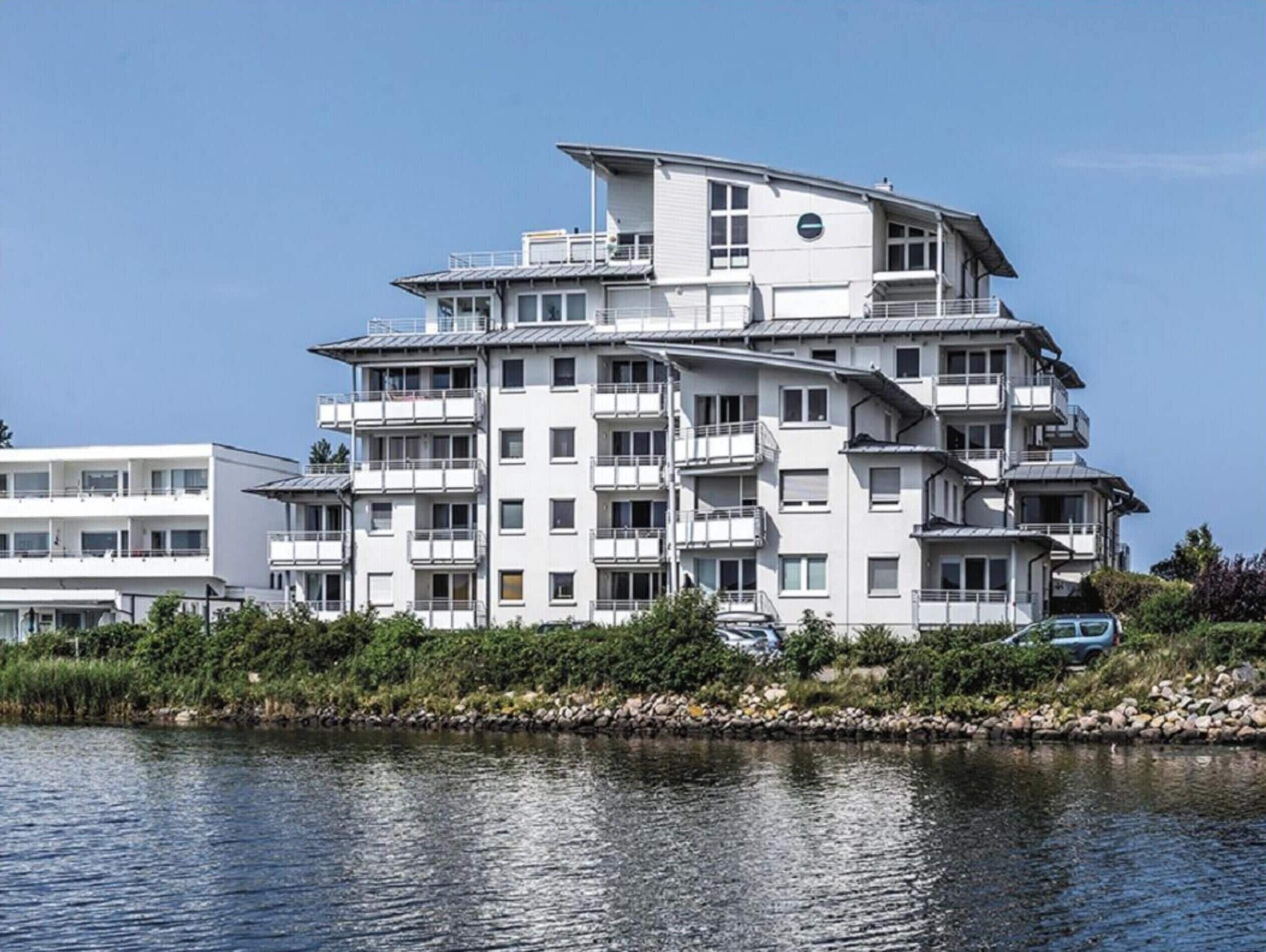 A multi-story residential building with balconies, situated by a body of water.