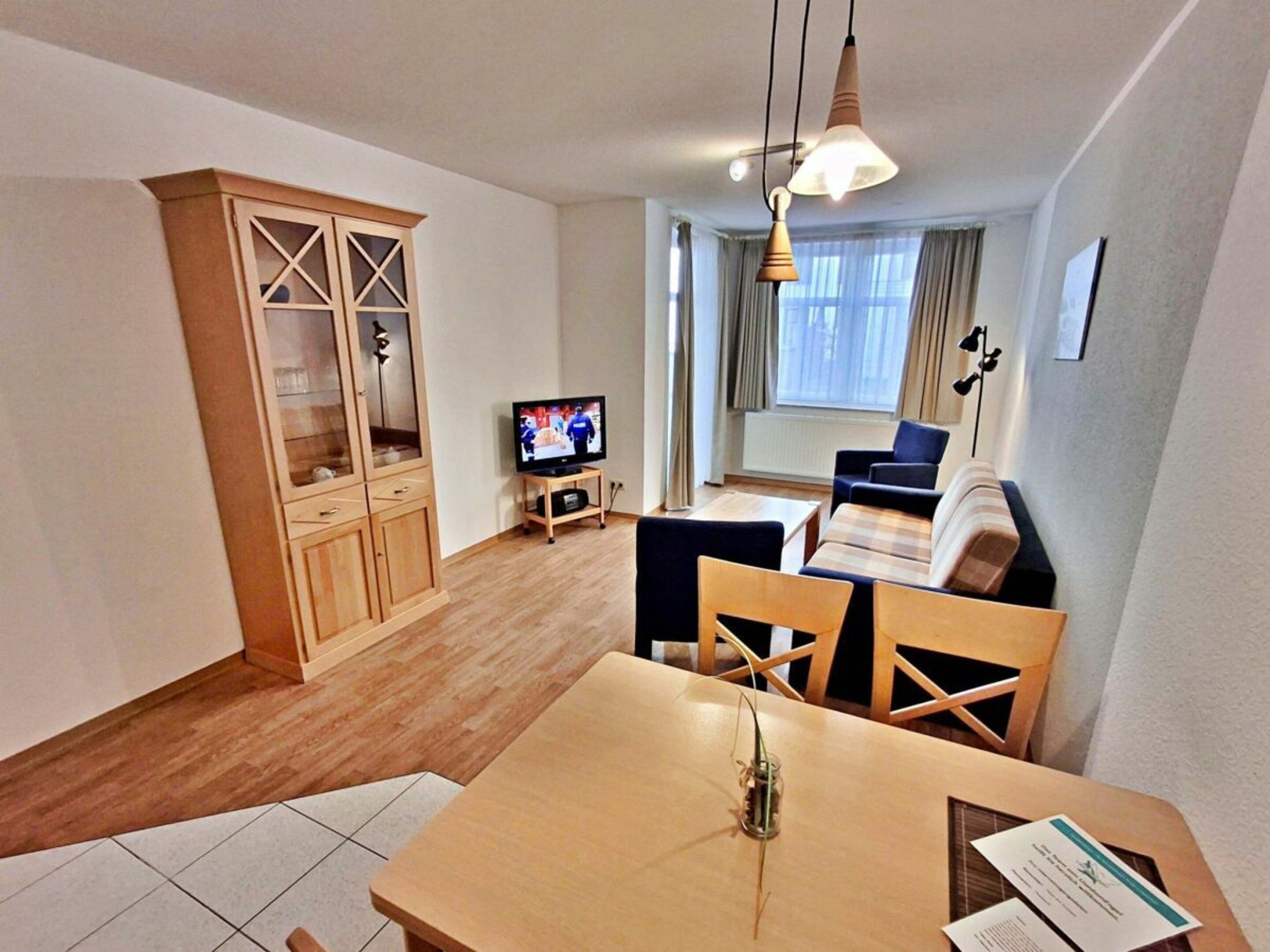 Una sala de estar moderna con televisión, muebles de madera y un comedor con mesa y sillas.