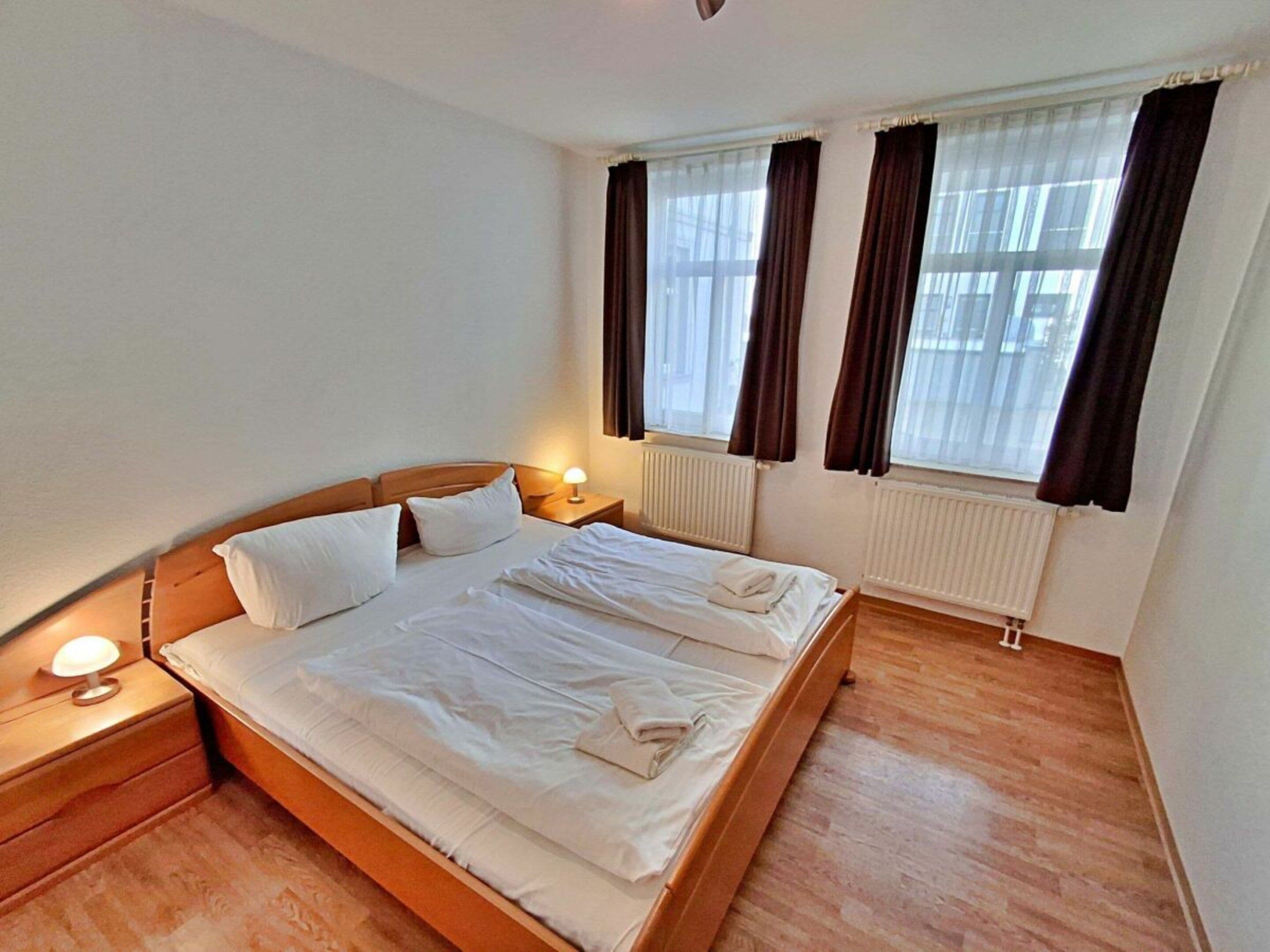 Habitación de hotel con cama doble, lámparas de noche, ventana con cortinas y un radiador.