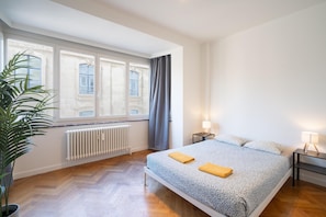 A bedroom with a large bed, two bedside tables with lamps, a radiator, and a window with curtains. - 3-bedroom Apartment Ideal for Families (Antwerp)