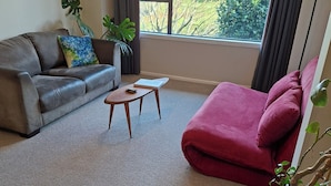 Sala de estar com sofá cinza, poltrona vermelha, mesa de centro de madeira e um vaso com planta.